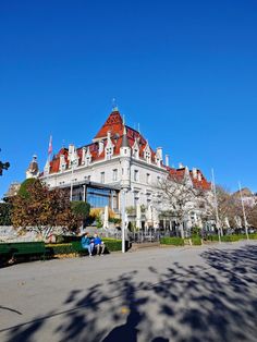 a large white building with red roof and two people sitting on the bench in front