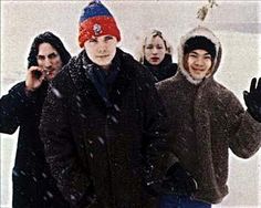 a group of people standing next to each other on top of snow covered ground with one person talking on a cell phone