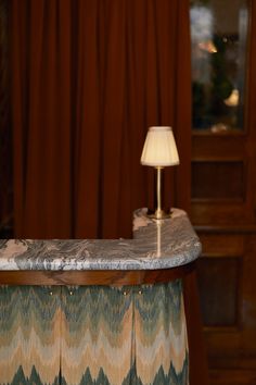 a table with a lamp on top of it in front of a curtained window