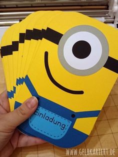 a hand holding four yellow and blue despicaded minion coasters in front of a kitchen counter