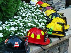 several fireman's hats are lined up on a stone wall next to white flowers