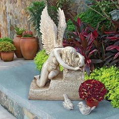 an angel statue sitting on top of a stone slab next to flowers and potted plants