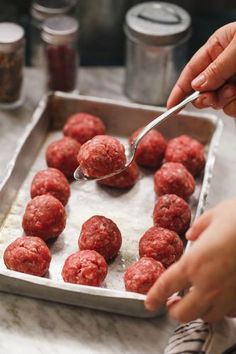 a person scooping some meatballs out of a baking pan with a spoon in it