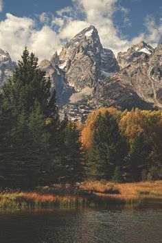 the mountains are covered in snow and trees with autumn foliage around them, near a lake