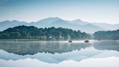 several small boats floating on top of a lake surrounded by mountains in the distance with fog