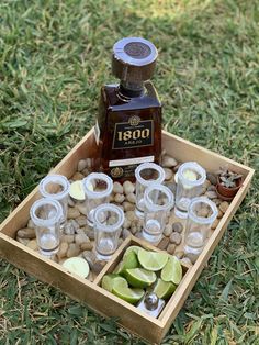 a wooden tray filled with shots and limes on top of rocks in the grass