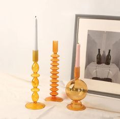 three candles are sitting on a table next to a framed photograph and two vases