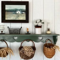 three baskets are hanging on a shelf in front of a painting and vases with flowers