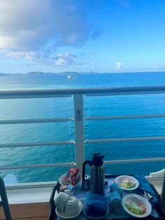 a table with plates and cups on it overlooking the ocean from a balcony in an apartment