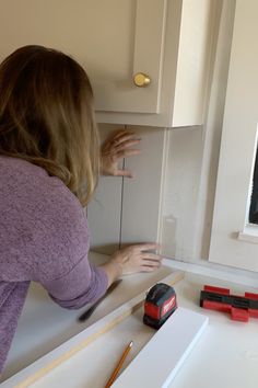 a woman in purple shirt working on kitchen cabinet door trimming and painting the cabinets