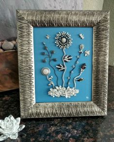 a silver frame with some flowers in it on a marble counter top next to a small white flower