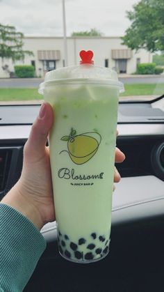 a person holding up a drink in their hand while sitting in a car with the steering wheel behind them