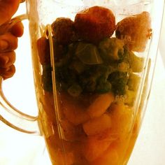 a blender filled with fruits and vegetables on top of a table next to a person's hand