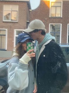 a man and woman standing next to each other in front of a building while holding a cell phone