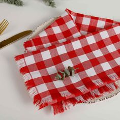 a red and white checkered table cloth with two small green leaves on it, next to a gold fork and knife