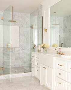 a white bathroom with marble counter tops and gold accents on the shower door, sink, and mirror