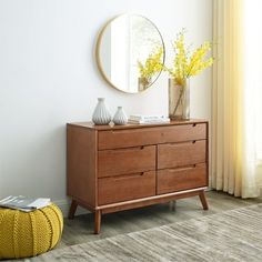 a wooden dresser sitting next to a window with yellow flowers on it and a round mirror