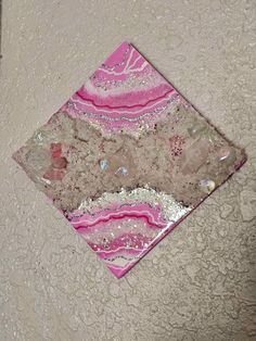 a pink and white square with some glitter on it's edges is hanging from the wall