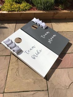 a white and black board with writing on it sitting on the ground next to some plants