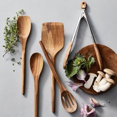 wooden utensils and spoons are arranged on a gray surface with herbs, mushrooms, and garlic