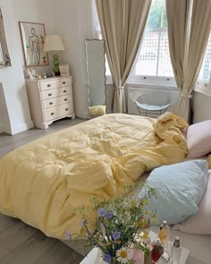 a bed sitting in a bedroom next to a window covered in yellow sheets and pillows