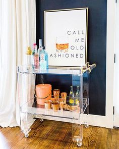 a clear bar cart with bottles and glasses on it in front of a black wall