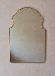 a mirror that is on the wall with gold trimmings and an arch shaped frame