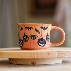 a ceramic cup decorated with bats and pumpkins is sitting on a wooden tray in front of a blurry background