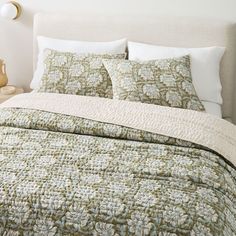 a bed with green and white bedspread, pillows and lamps on the side