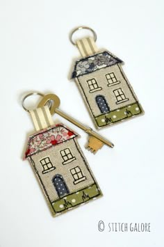 two house keychains with keys attached to them on a white surface, one has a gold key in it and the other is made out of fabric