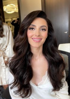 a woman with long dark hair sitting in front of a mirror and smiling at the camera