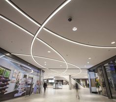 people are walking around in the lobby of an office building with curved ceilinging and lighting