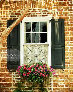 a window with green shutters and red flowers in the window box next to it