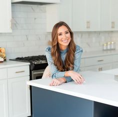 a woman sitting at a counter in a kitchen with white cabinets and blue counterstop