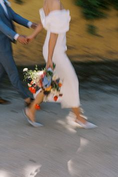 a bride and groom walking down the street holding hands with flowers in their bouquets