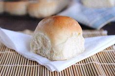 a roll sitting on top of a white napkin next to some rolls in the background