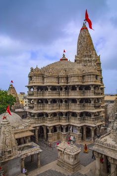 an elaborately carved building with flags flying in the wind and people walking around it