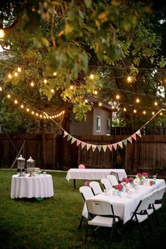 an outdoor party is set up with white tablecloths and lights strung from the trees