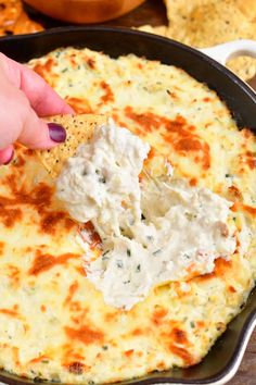 a hand dipping a tortilla chip into a skillet filled with dip and cheese