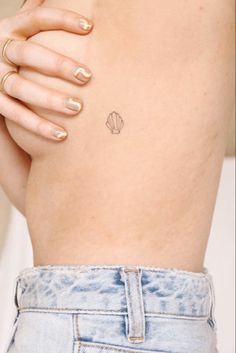 a woman's stomach with a small shell tattoo on her left side ribcage