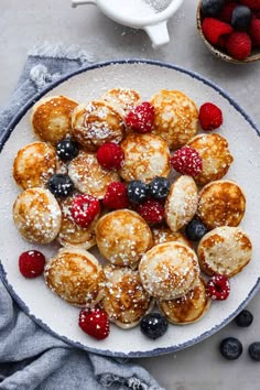 a white plate topped with pastries covered in powdered sugar and berries next to a cup of coffee