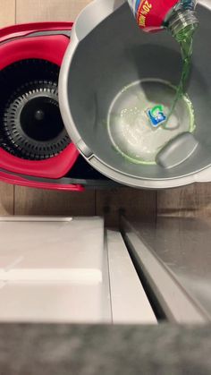 a person pouring water into a red and silver container on top of a stovetop