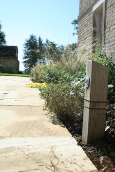 a wooden pole sitting in the middle of a garden next to a brick building and bushes