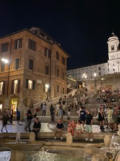 many people are walking up and down the steps in front of some buildings at night