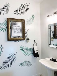 a bathroom with palm leaves painted on the wall and a mirror over the sink in front of it