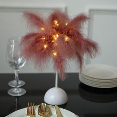 there is a table set for two with goldware and pink feathers on the place setting