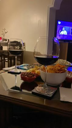 a glass of red wine sitting on top of a table next to a bowl of food