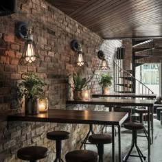 a brick wall with several tables and stools in front of it, surrounded by potted plants