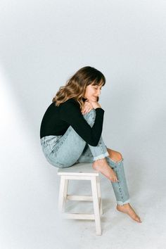 a woman sitting on top of a white stool with her legs crossed and looking off to the side