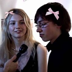 two people standing next to each other with hair clips on their head and one person holding a microphone